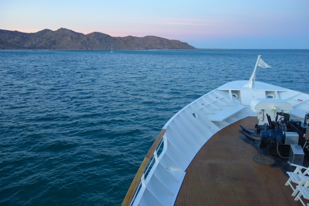 Bow of the Uncruise small ship cruise sailing in the ocean of Baja with mountains.