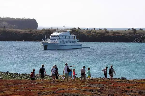 Family charter group walking on the shore in front of their small ship in the Galapagos Islands