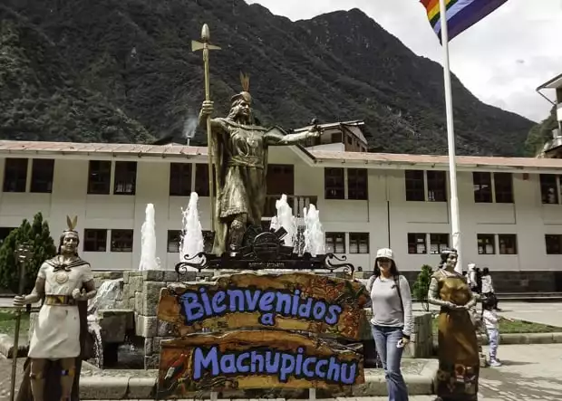 Happy guest on tour to Machu Picchu standing next to the Bienvenidos sign. 
