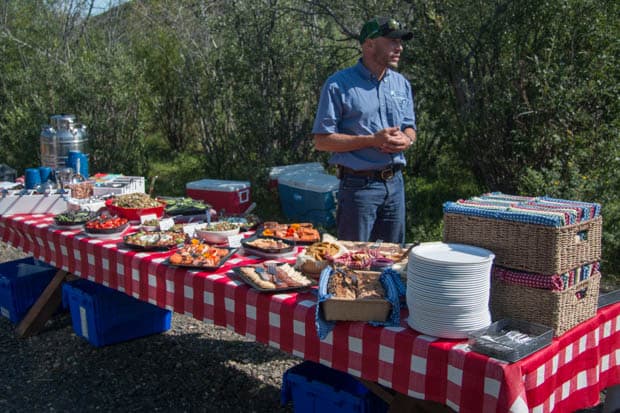 A man standing in front of a picnic table set with a lunch spread. 