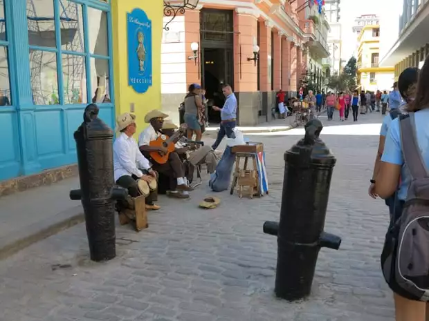 Locals sitting on the sidewalk curb playing music in Havana Cuba. 