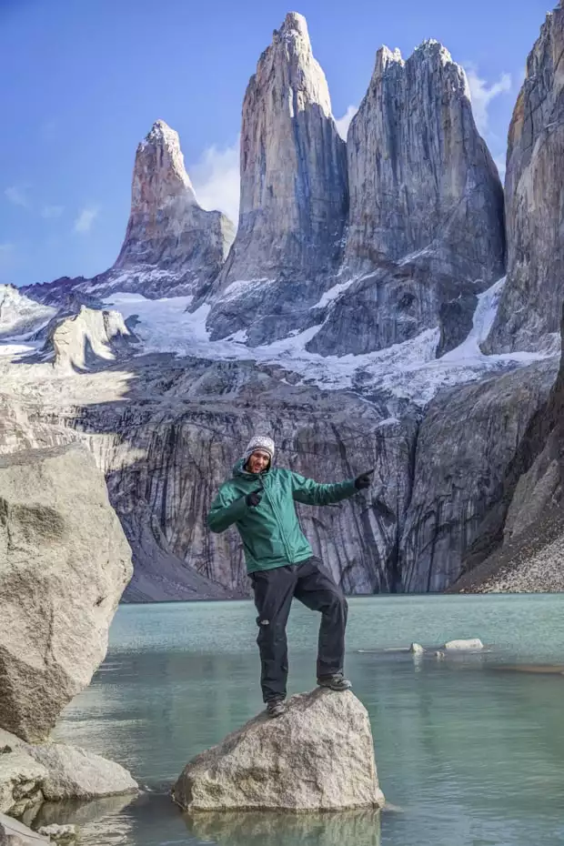 Happy traveler pointing while standing on a rock in the lake below large granite towers in Patagonia.
