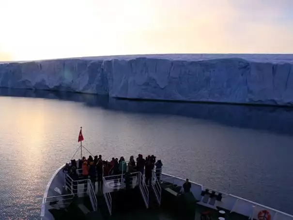 Group of small ship travelers on the bow of the M/S Expedition looking a massive tidewater glacier wall.