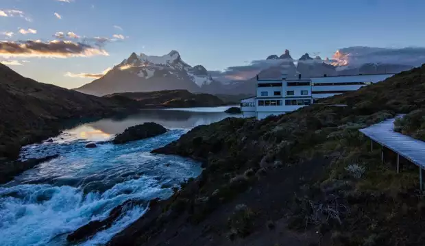 Explora Lodge set on a hillside next to the shore of Lake Pehoe on a Patagonia land tour with snow capped mountains in the background.