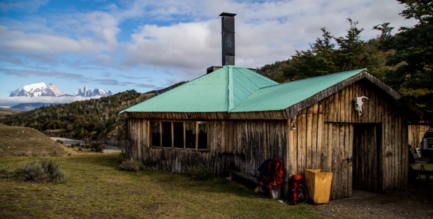 Wooden cabin set in a green valley floor in Patagonia.