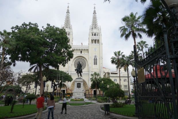 Cathedral in Guayaquil outside of a green park with cobblestone walkway and people milling about.