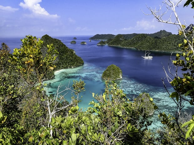 A small ship anchored in turquoise waters among several islands in Indonesia.
