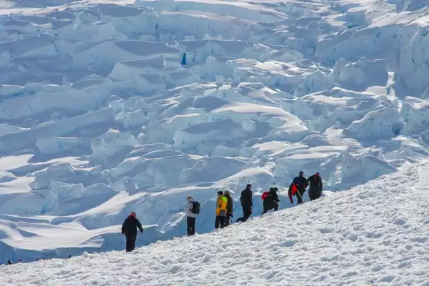 Guests from a small ship on a hiking excursion in Antarctica with only white snow formations in the background. 