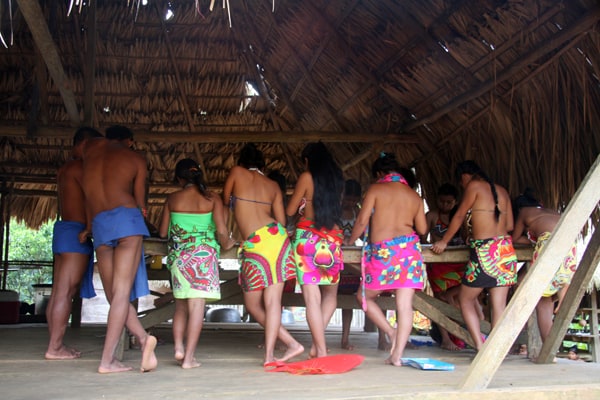 Native locals of a remote village in the jungle around a table underneath a thatched roof hut.