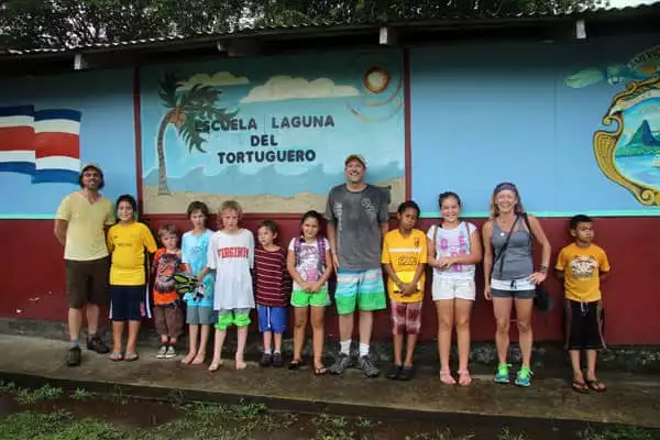 Families of travelers and local community kids posing in front of a school.