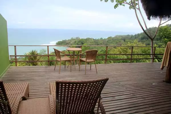 View of a deck with chairs and tables located atop the Costa Rican rainforest and the ocean.