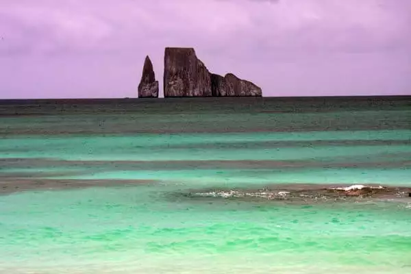 Sunset view from the beach of granite spire and rock formations in the ocean with green ocean water on the shoreline in the Galapagos.