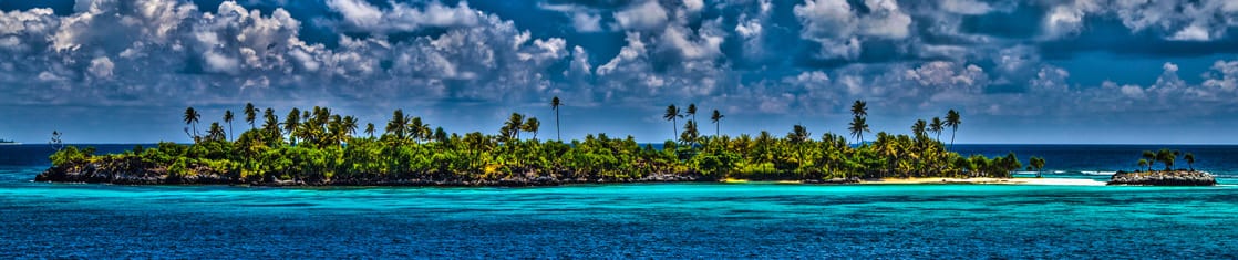 Small island with palm trees in the South Pacific seen from a small cruise ship. 