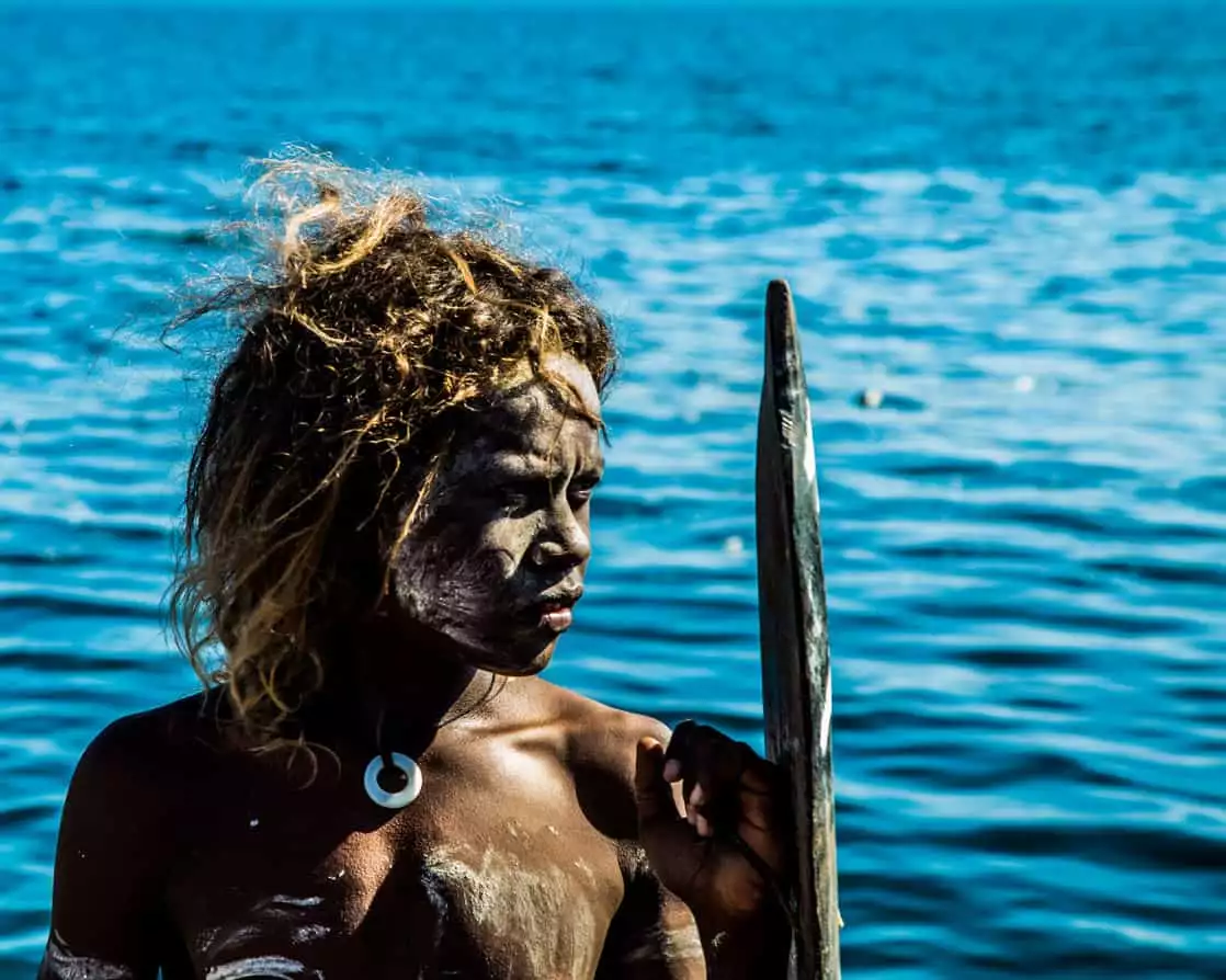 Local warrior in a community in the South Pacific islands with painting on his body and the ocean in the background.