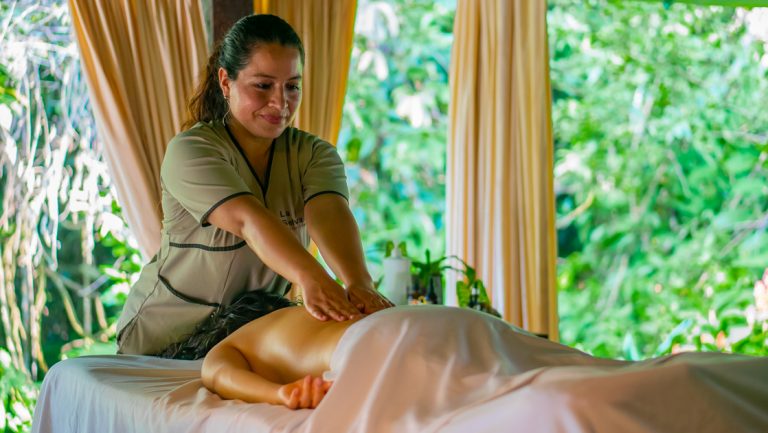 Woman gives a massage to a guest of La Selva Lodge in Ecuador in outdoor, covered area with jungle & beige curtains.