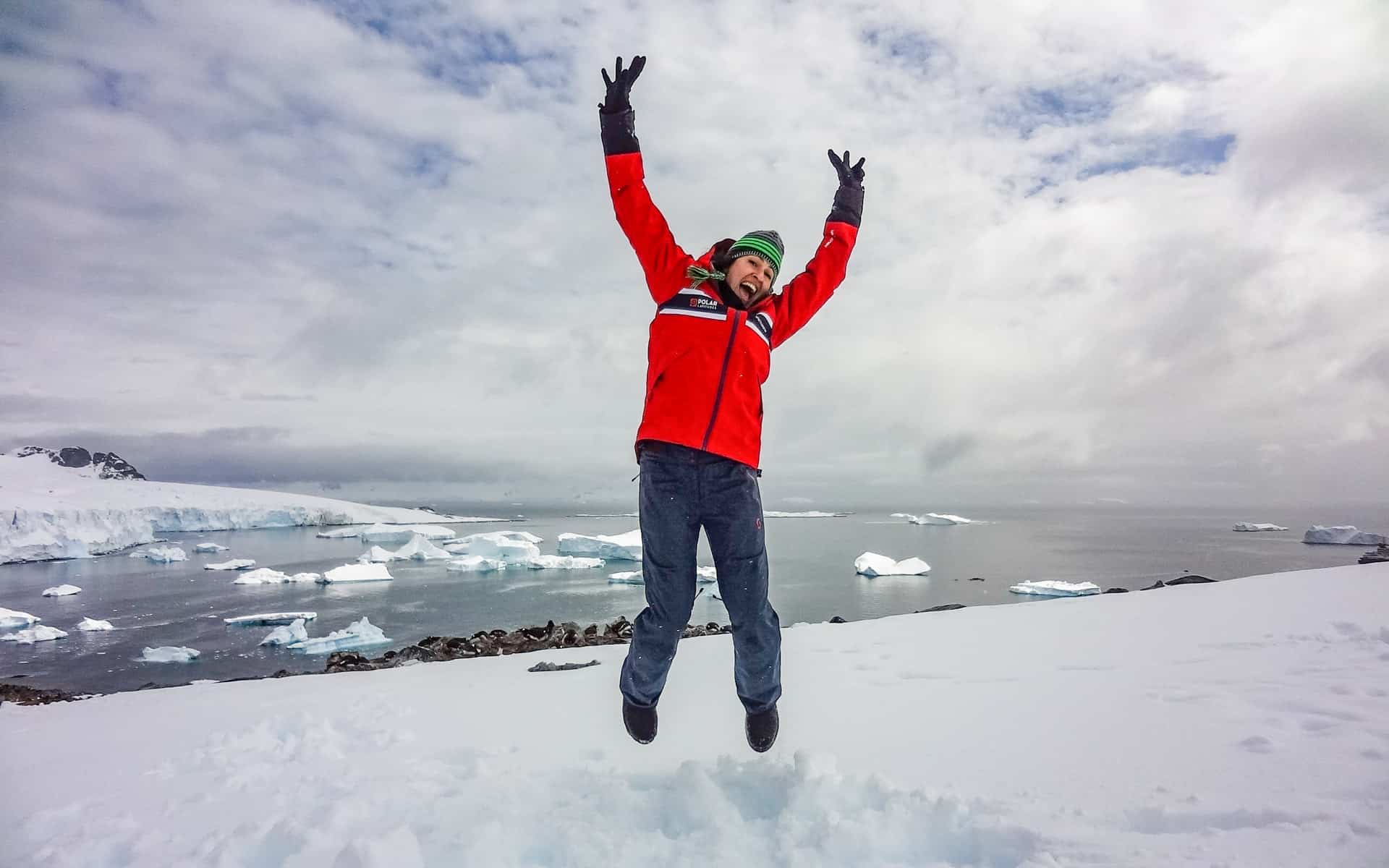 Solo woman traveler jumping on a snow hill overlooking Antarctica's coastline.