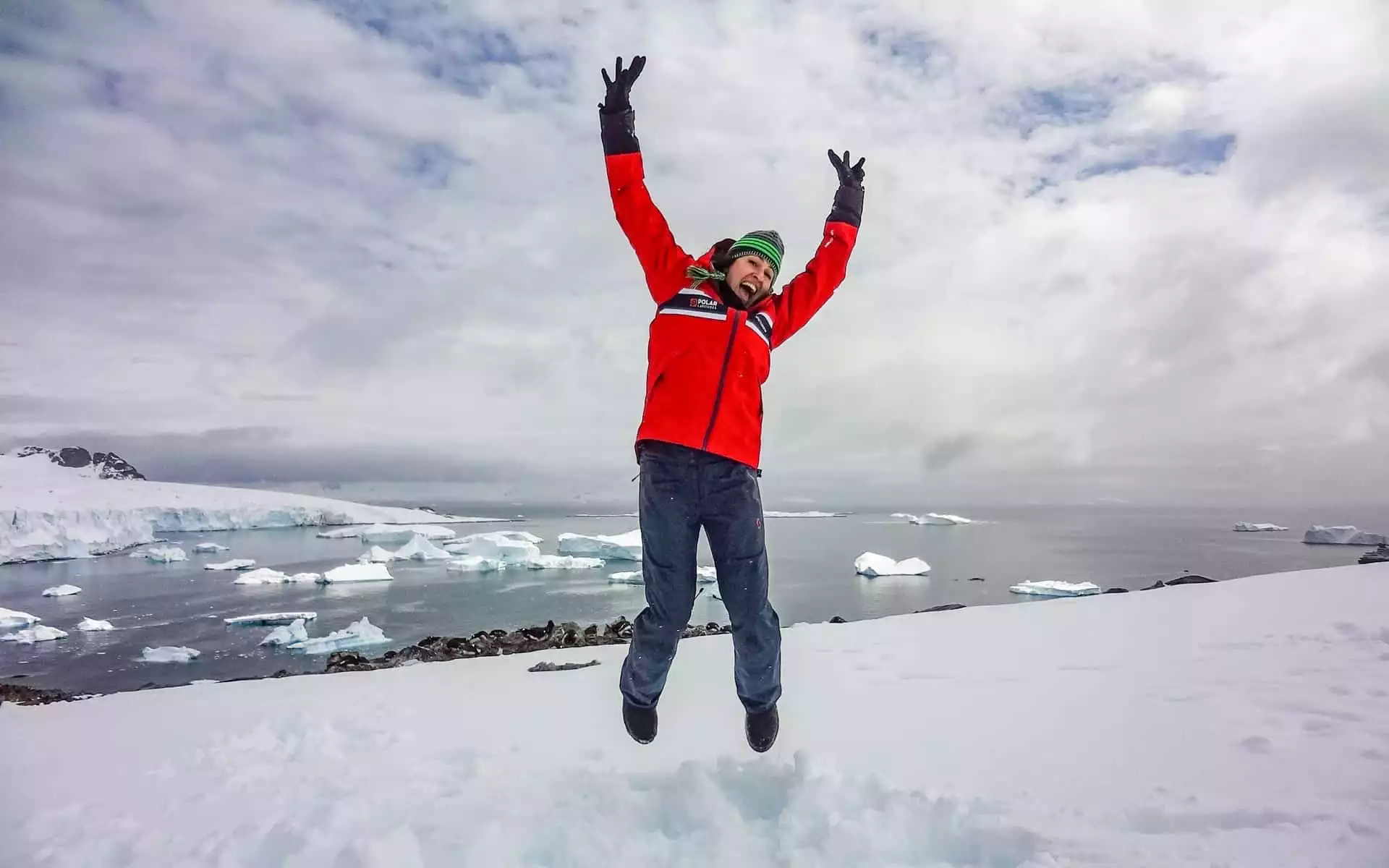 Solo woman traveler jumping on a snow hill overlooking Antarctica's coastline.