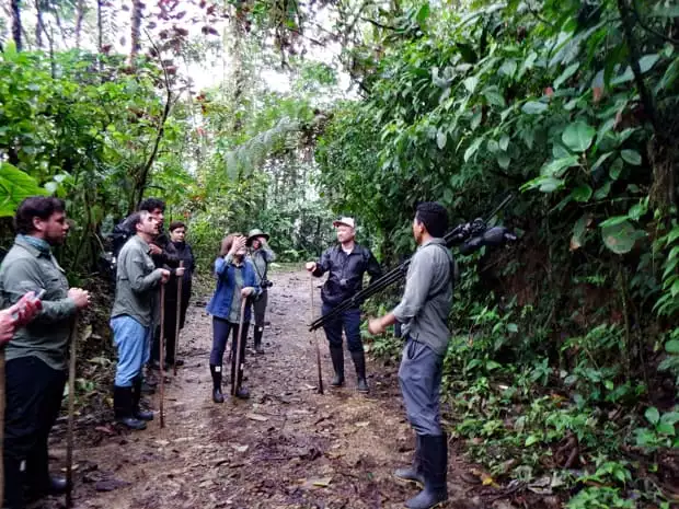 Group of travelers in Ecuador walking on a muddy trail in the rainforest with a guide.