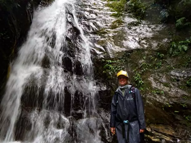 A traveler in Ecuador standing next to a waterfall with green moss on granite rocks.