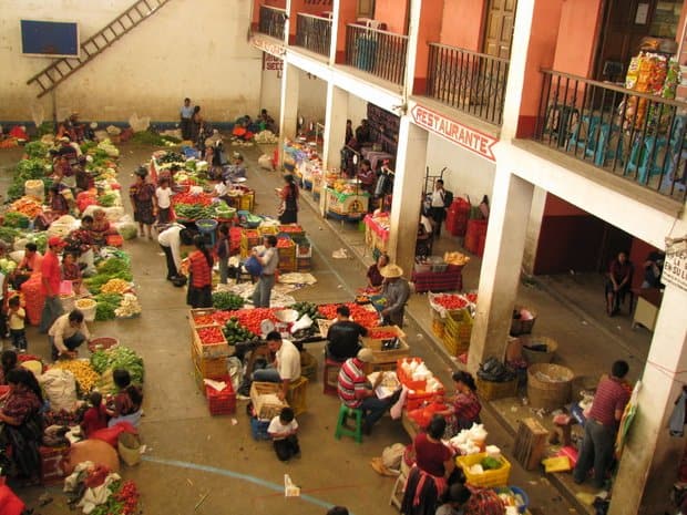 Local fruit and vegetable market bustling with people in a courtyard of building.
