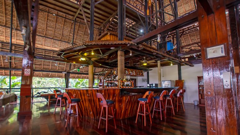 Open-air bar at Napo Wildlife Center with carved wood exterior & barstools & wine racks within large thatched-roof building.