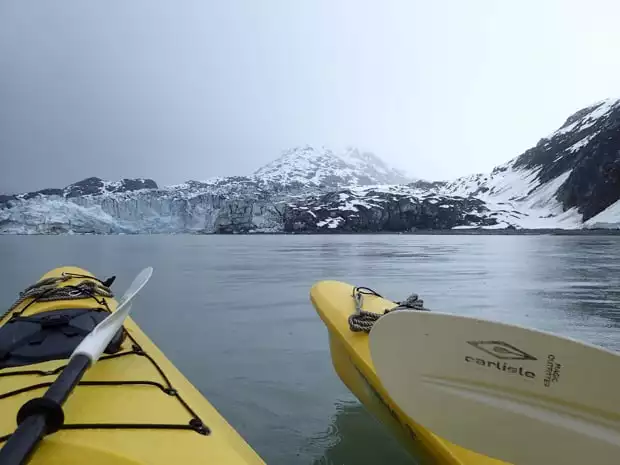2 kayaks floating on the water in Alaska in front of a tidewater glacier.