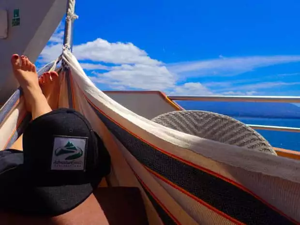 Galapagos passenger on the small ship cruise Origin relaxing in a hammock on a balcony deck enjoying the view of the ocean and outlying islands.