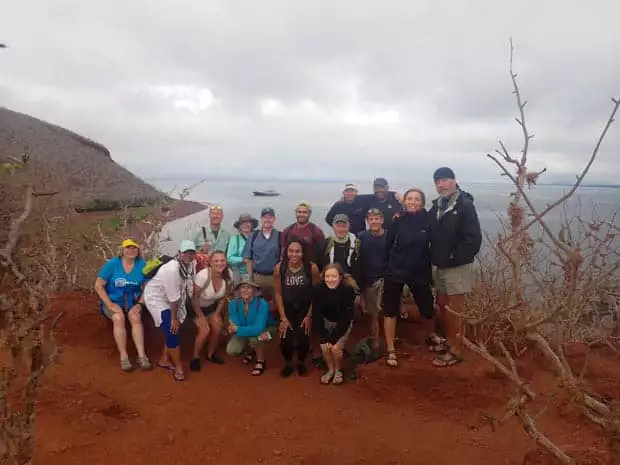 Group of happy travelers on a bluff with on a Galapagos Island hike with the Origin in the background.