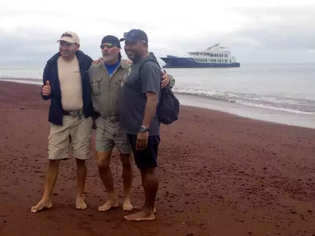 Origin crew on the beach with the small ship cruise Origin anchored off the shoreline.