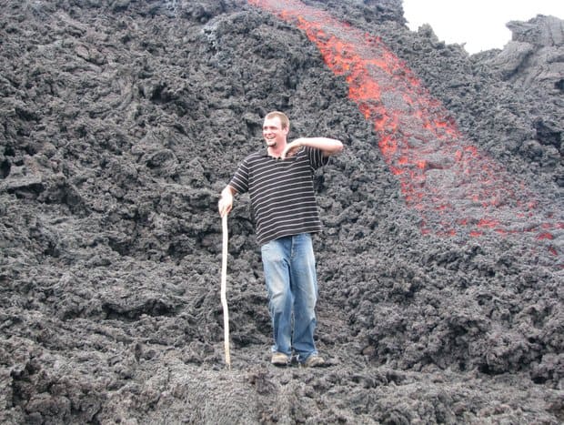 Happy young traveler walking down volcanic rock with hot lava running underneath volcanic rock next to him.