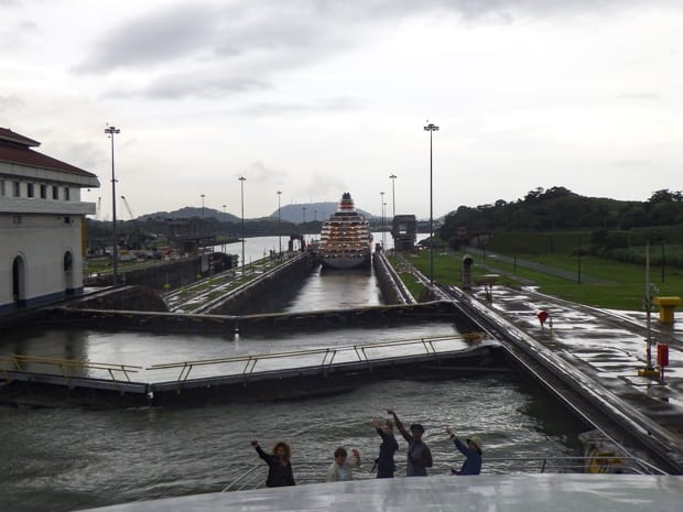 People waving from the bow of a small ship cruise going through the locks in the Panama Canal. 