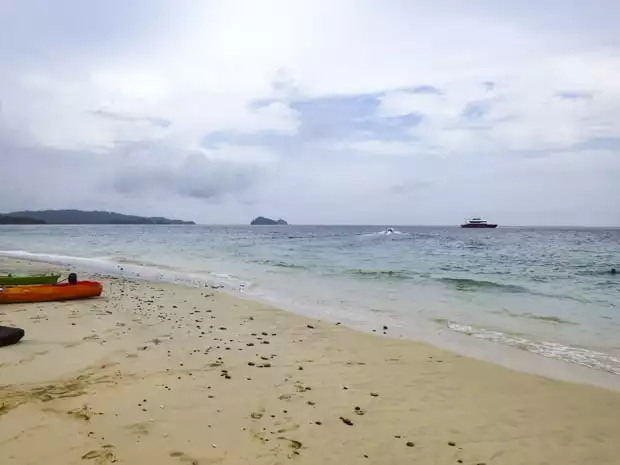 Kayaks resting on the beach at the pearl islands with a small ship in the background. 