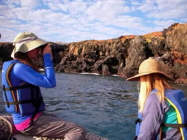 2 travelers viewing the rocky, colorful shoreline from the zodiac in the Galapagos.
