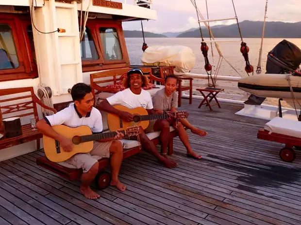 Three crew members playing guitar and singing on deck aboard the small ship Ombak Putih. 