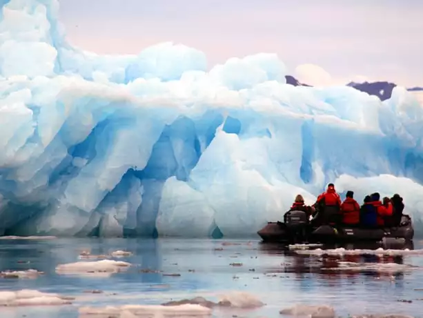 Group of Arctic travelers in a zodiac looking at a giant iceberg.