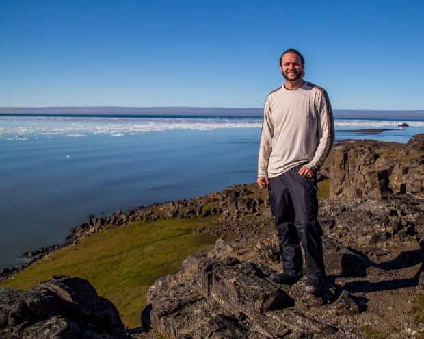 A man sanding on a cliff overlooking the Arctic ocean on a sunny day