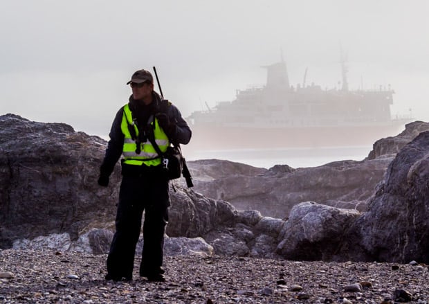 A cruise guide standing watch on shore with a small ship in the background
