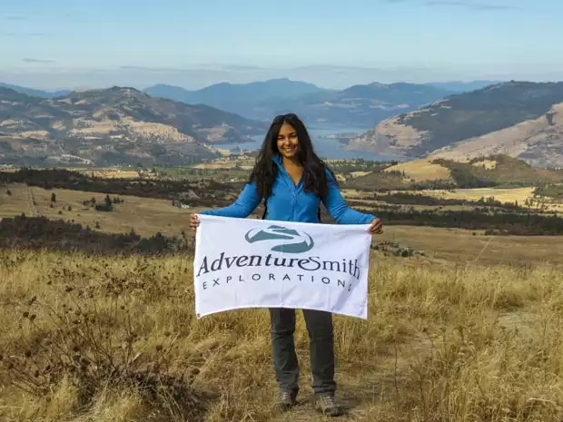 Guest posing with an AdventureSmith Explorations flag at a viewpoint on their hike in the Pacific Northwest. 