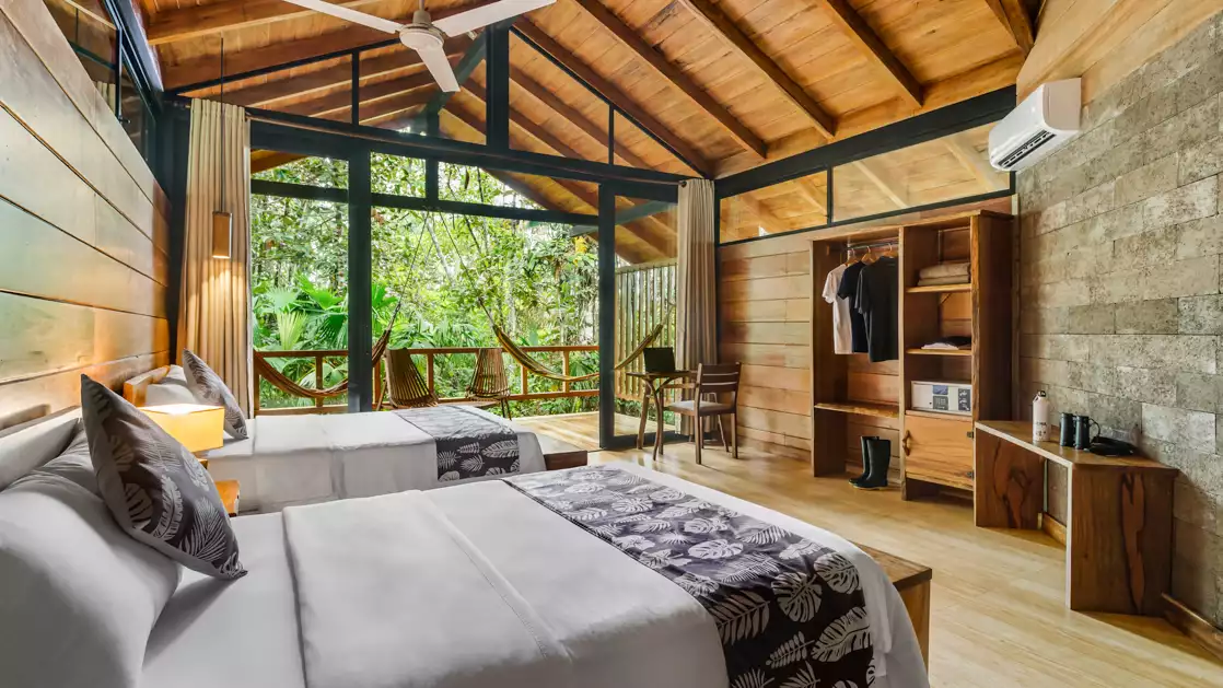 Two double beds with crisp linens in a room featuring a balcony with hammocks and closet desk and a great view of the jungle