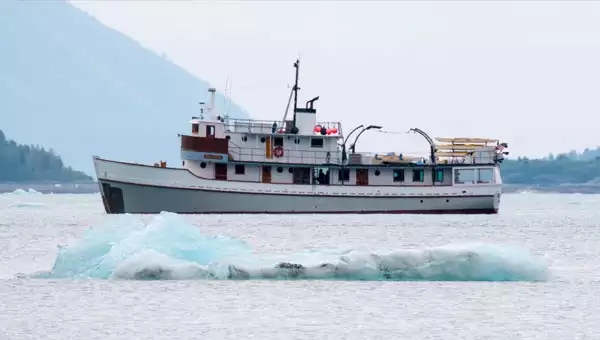An 8-guest adventure yacht sails behind a blue iceberg in Alaska