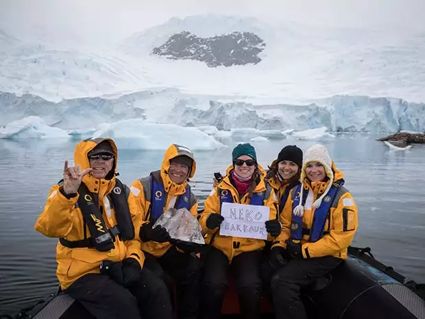 Guests from a small ship on a skiff excursion in Neko Harbor, Antarctica holding up signs and smiling. 