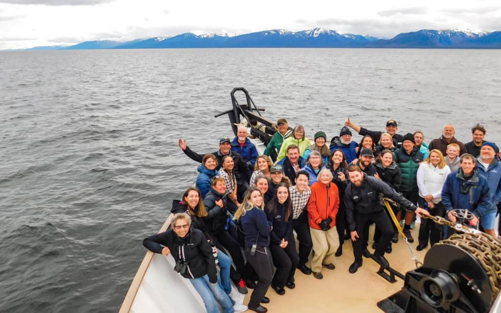 A group of Alaska travelers on the bow of the Wilderness Adventurer smiling for the camera at the end of a small ship cruise through alaska.
