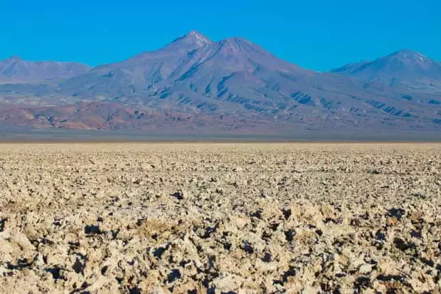 A desert view of rough ground with mountains in the background.