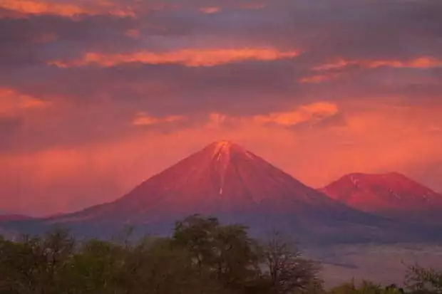 A volcano with the sun setting on the peak creating a pink sky and pink mountains in Atacama, Chile