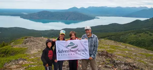 A family holding a flag above at the top of a hill in Alaska. 