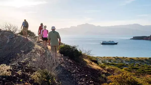 group of people hiking on a land tour with a small ship in the background