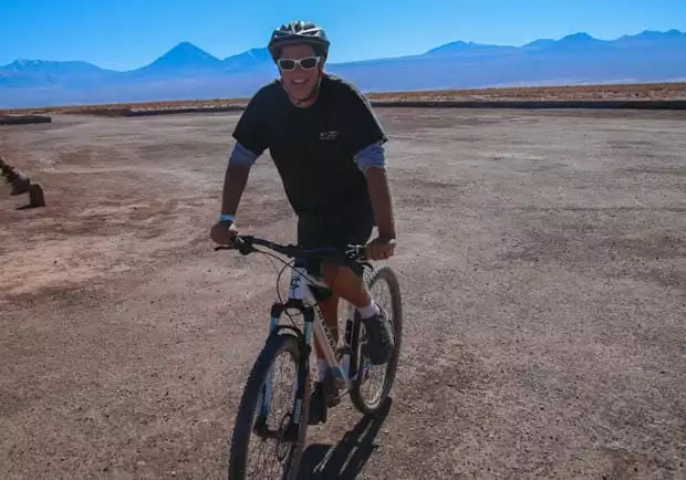 A Chile traveler riding a mountain bike over the desert and smiling.