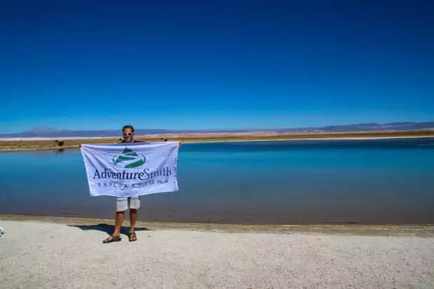 Author standing with AdventureSmith flag in front of a salt lake in the Atacama Desert in Chile.