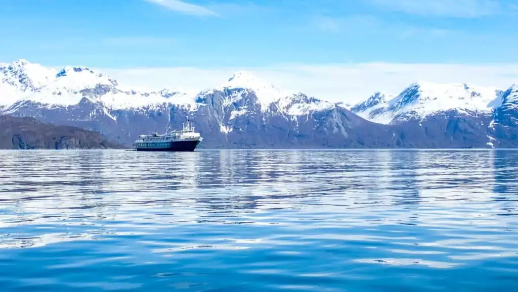 A reflection on the blue water of the snow capped mountain range and the alaska small ship -wilderness adventurer floating on the horizon 