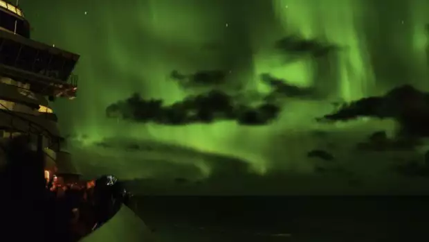 Green northern lights in the night sky viewed from the deck of a Alaskan small ship cruise.